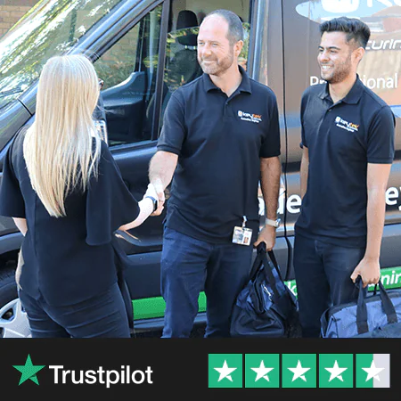 Two professionals in black polos shake hands with a woman outside a branded locksmith van, with equipment bags in hand.