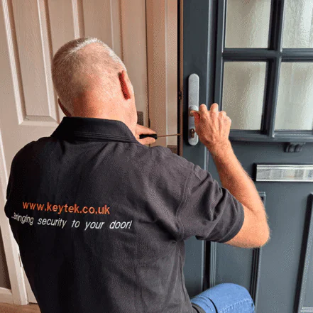 A locksmith in a black shirt repairs a door lock, using tools outside a home, emphasizing security services.