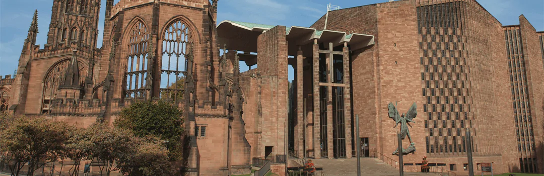 Full view of Liverpool Cathedral captured during daylight, highlighting the contrast between its historic reddish-brown stone architecture with arched windows on the left and the modern glass-and-metal extension on the right; framed with surrounding greenery and soft natural lighting to emphasize the blend of traditional and contemporary design.