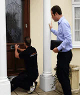 locksmith working on door with customer stood close by