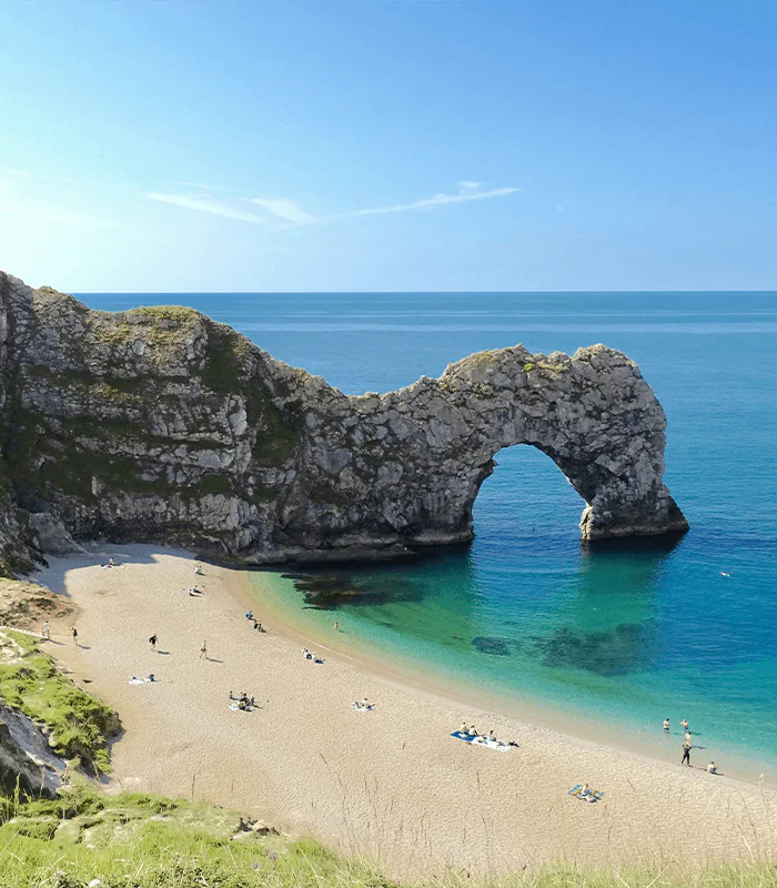 A tranquil beach scene features the iconic Durdle Door rock arch, with sunbathers on golden sands and turquoise waters under a clear blue sky.