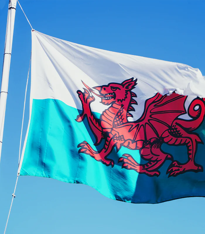 The flag of Wales featuring a red dragon on a green and white background, fluttering against a clear blue sky.