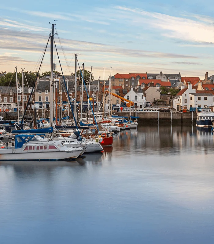 Tranquil harbor scene with moored boats, serene water reflections, and quaint buildings against a calm sky at sunset.