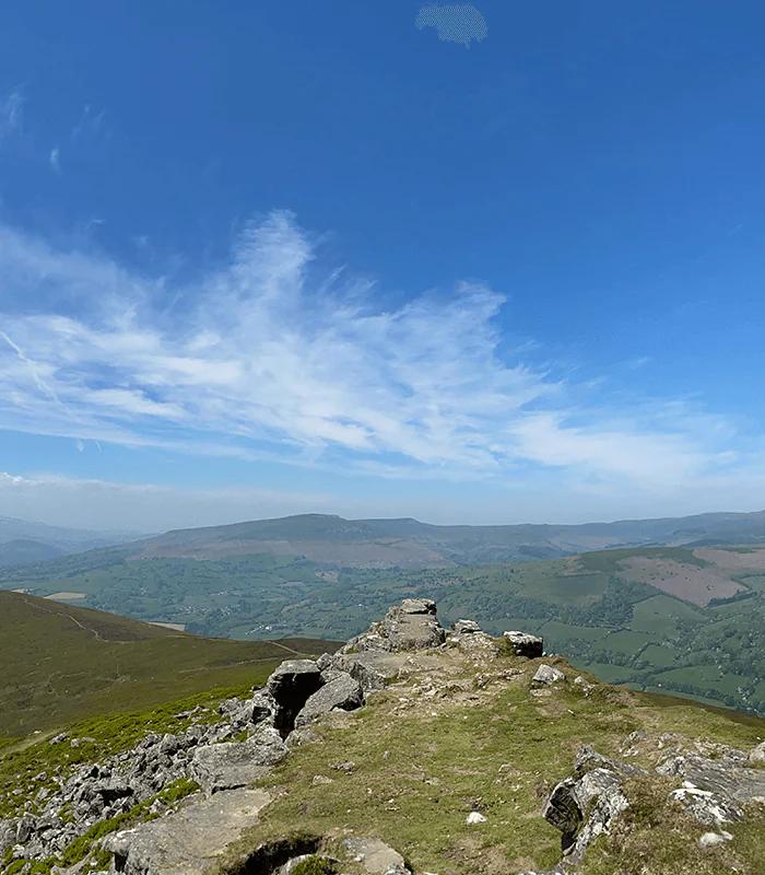 A panoramic view of rolling green hills under a bright blue sky, with rocky outcrops lining a ridge. Ideal for hiking or nature walks.