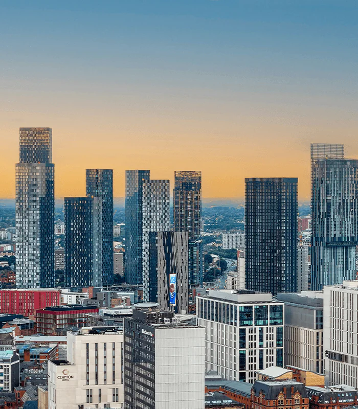 A panoramic view of modern skyscrapers in Manchester at sunset, showcasing a blend of glass and steel structures against a colourful sky.