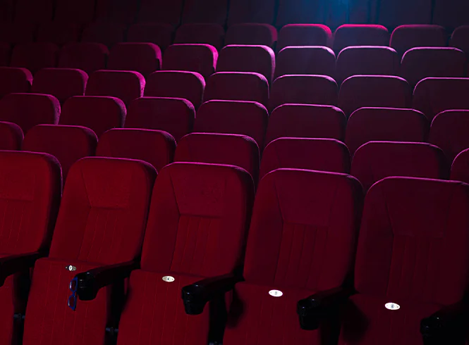 Rows of plush red theater seats illuminated by soft light, creating an inviting ambiance in a cinema hall.