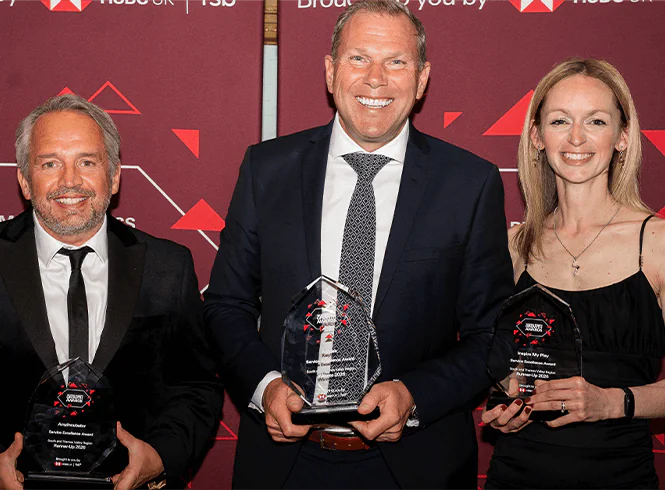 Three people in formal attire holding awards against a red backdrop with logos and geometric designs.